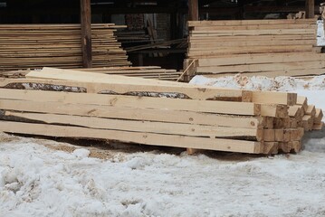 a pile of brown long wooden planks and beams on white snow on a winter street