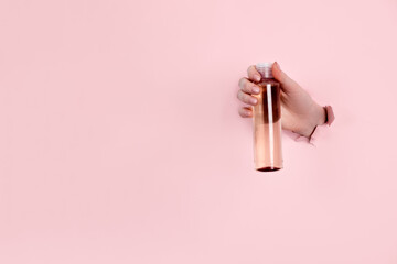 Glass Bottle in female hand with fluid collagen and hyaluronic acid, hydration skin. Copyspace Abstract pink background.