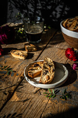 Homemade almond and chocolate biscotti with glass of coffee and  ranunculus flowers on wooden table on dark background.