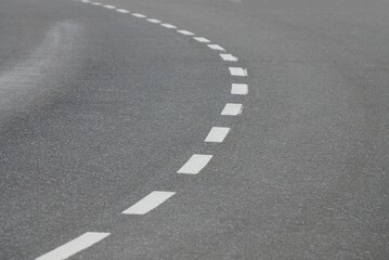 part of a gray asphalt road at a bend with white striped markings