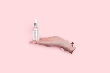 Glass Bottle in female hand with fluid collagen and hyaluronic acid, hydration skin. Copyspace Abstract pink background.