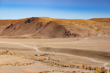 Scenic view over rural road, surrounded by hills, overgrown by dried grass in the mountains in Kyzyl-Chin valley aka Mars. Altai autumn landscape, Russia