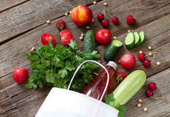 Disposable paper shopping bag with veggies, fruit, berries, herbs, juice on wooden background