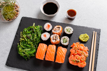 Sushi takeaway with sushi set, wakame salad, chopsticks and sauces on gray concrete background, top view
