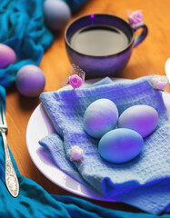 Obraz na płótnie Canvas Easter eggs in a white plate, painted with pastel colors. A cup of black coffee on a wooden table.