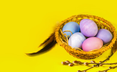 Easter painted multicolored eggs in a wicker basket on a yellow background with copyspace