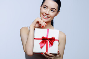 Cheerful woman holding present box in studio on gray background. Smiling beautiful young girl expressing happy emotions. Seasonal discounts and sale. 