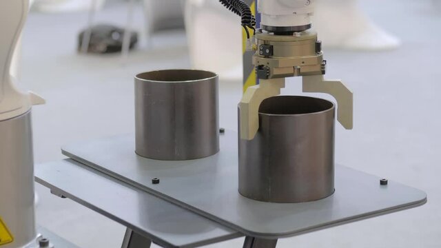Pick and place industrial robotic clamp arm manipulator moving cylindrical metal workpiece at modern robot exhibition, trade show - close up view. Manufacturing, engineering, ai, technology concept
