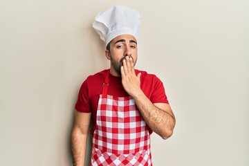 Young hispanic man wearing baker uniform bored yawning tired covering mouth with hand. restless and sleepiness.