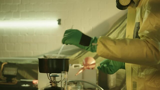 Illegal chemist cooks drugs in underground laboratory wearing mask and works with toxic chemical compounds