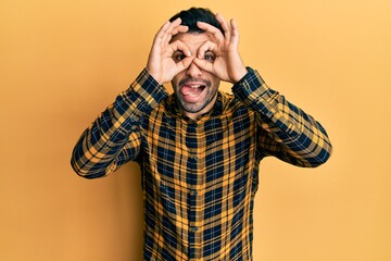 Young hispanic man wearing casual clothes doing ok gesture like binoculars sticking tongue out, eyes looking through fingers. crazy expression.