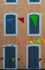 multi colour  celebration flags or bunting hanging in french street with colorful facade and shutters ,focus on flags .