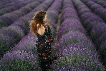 Beautiful young woman portrait in lavender field. An attractive girl with long curly hair in a long dress is dreaming.