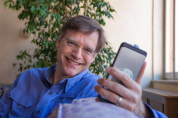 Smiling Caucasian man in forties holding smartphone by window indoors
