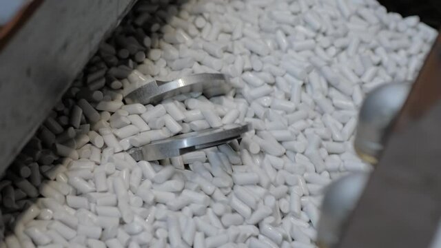 Tumble finishing process at factory - automated trough vibrator machine polishing metal workpieces by abrasive stones - close up. Metalworking, industrial, equipment, technology, manufacturing concept