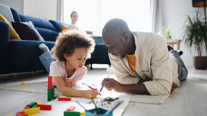 Father with small daughter drawing pictures, multi ethnic family and home office.