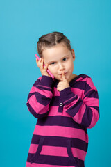 close-up portrait of a mysterious girl with pigtails making a phone call and holding a finger to her mouth, a secret or a request for silence, isolated on a blue background.