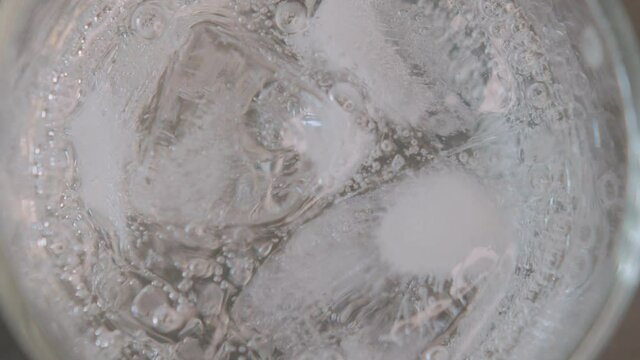 Pouring soda water into a glass with ice cubes, close-up top view with splashes and drops