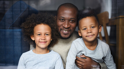 Father with small children looking at camera at home, multi ethnic family.