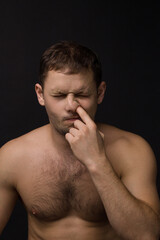 Man picks his nose on a black background. Muscular and athletic. Portrait of a man. Male model in studio