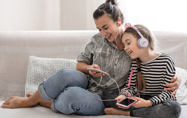 A young mother and her daughter are listening to music on their phones while sitting on the couch...