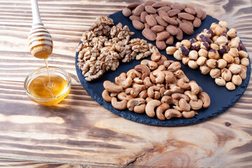 Various nuts sorted in glass bowl with honey bowl and honey dipper