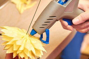 Woman make floral design. Girl glues the petals of an artificial flower using a glue gun. Close-up,...