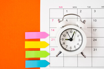 white alarm clock on opened calendar with paper tag ,  on grunge orange paper background