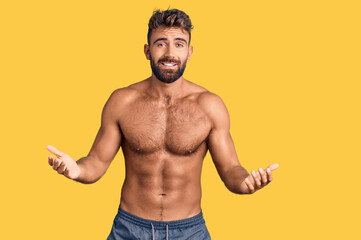 Young hispanic man wearing swimwear shirtless clueless and confused expression with arms and hands...