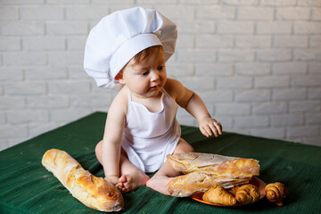 Little boy in a cap and with bread. Little child dressed as a cook in the kitchen.