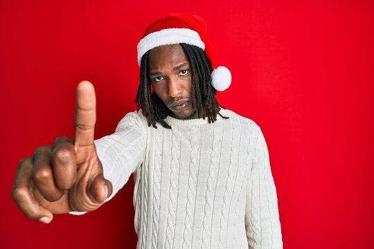 African american man with braids wearing christmas hat pointing with finger up and angry expression, showing no gesture