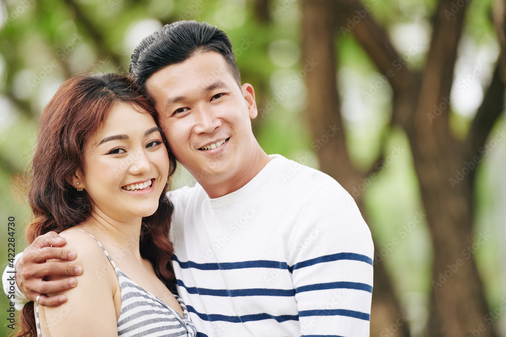 Poster portrait of happy hugging young asian boyfriend and girlfriend smiling and looking at camera