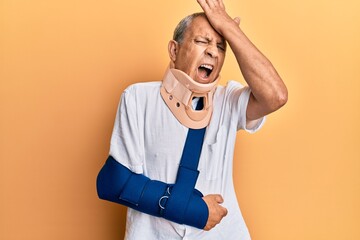 Handsome mature senior man wearing cervical collar and arm on sling surprised with hand on head for...