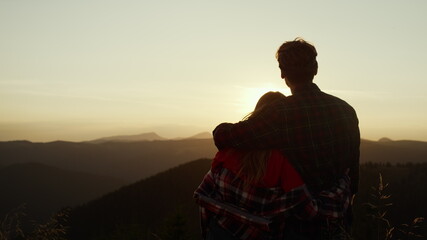Couple looking sun setting behind mountain. Loving man and woman enjoying sunset