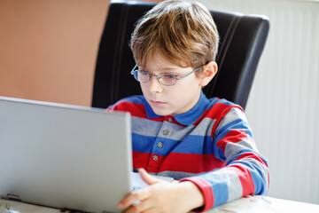 Happy healthy kid boy with glasses making school homework at home with notebook. Interested child writing essay with helping of internet. concetrated schoolchildren concept