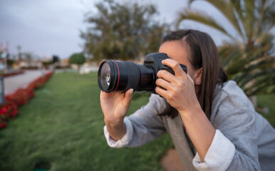 The girl makes a photo on a professional camera in the garden among the palms.