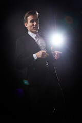 Portrait of an attractive young man in a black suit on a dark background with lighting in the studio