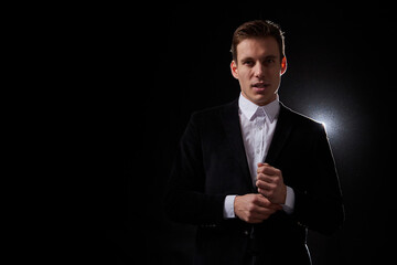 Portrait of an attractive young man in a black suit on a dark background with lighting in the studio