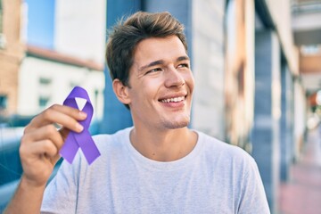 Young caucasian man smiling happy holding purple ribbon at the city.