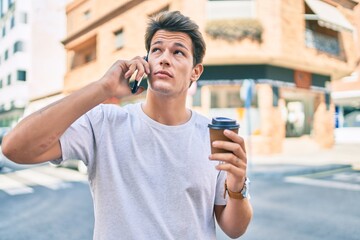 Young caucasian man with serious expression talking on the smartphone and drinking coffee at the city.