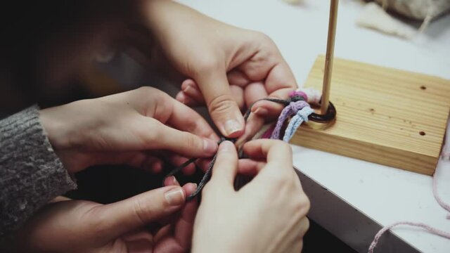 Mom or teacher helps the child weave macrame. Hands close up. Family hand made pastime