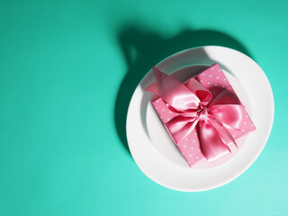 A gift box with a pink ribbon lies on the plates saucers on a mint-colored background.