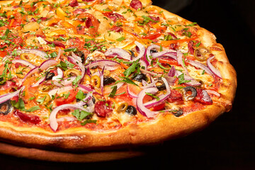 Pizza with cheese, sausages, tomatoes, olives and onions on a wooden board. Close-up, selective focus.