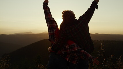 Couple looking sunset over mountain. Happy woman and man raising hands in air