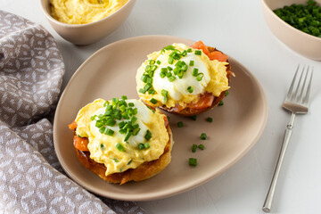 Delicious hearty breakfast, eggs Atlantic in a plate on a white background, round fried bun with salmon and eggs Benedict, hollandaise sauce and green onions