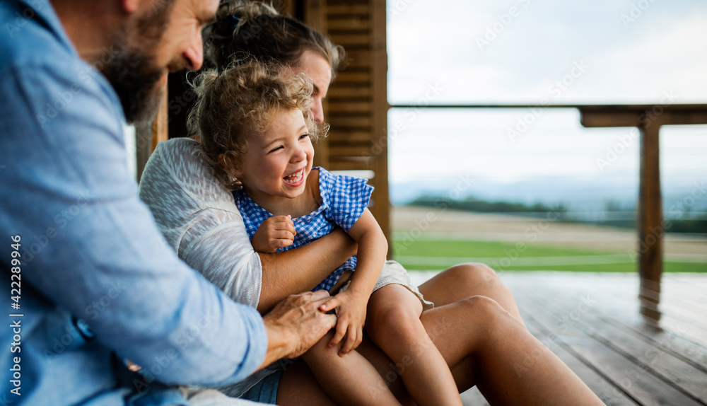 Wall mural Family with small daughter sitting on patio of wooden cabin, holiday in nature concept.