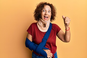 Beautiful middle age mature woman wearing cervical collar and arm on sling screaming proud,...