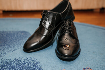 Gold wedding rings on black shoes on the floor. Accessories for the groom on the wedding day