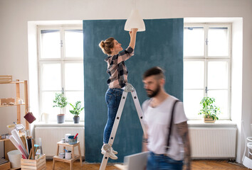 Mid adults couple changing light bulb indoors at home, relocation and diy concept.