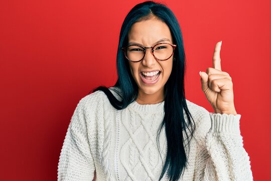 Beautiful hispanic woman wearing casual sweater and glasses pointing finger up with successful idea. exited and happy. number one.